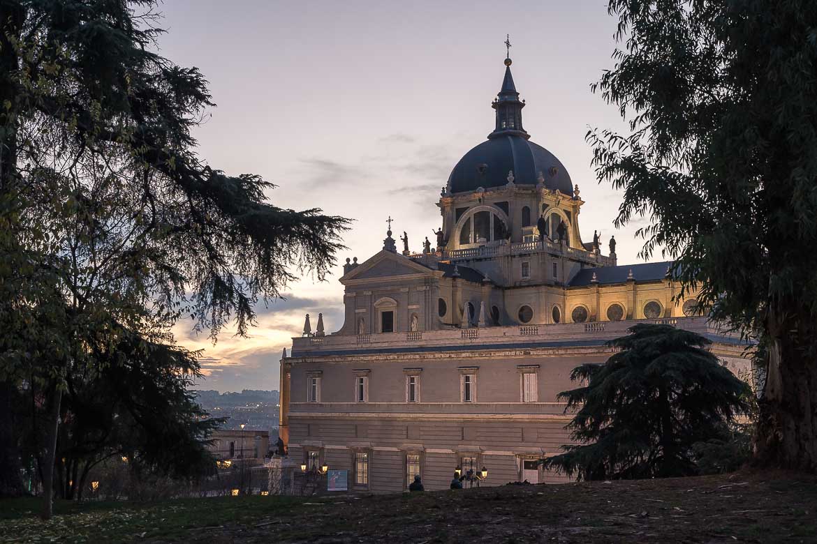 This image shows the exterior of the Almudena Cathedral at dusk. 
