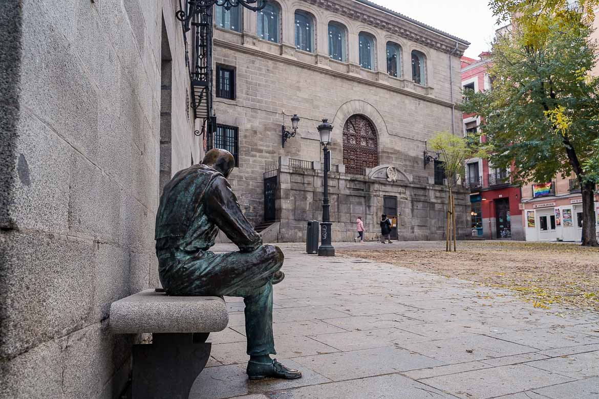 This image shows a sculpture of a man sitting on a bench in Plaza de la Paja in La Latina district.