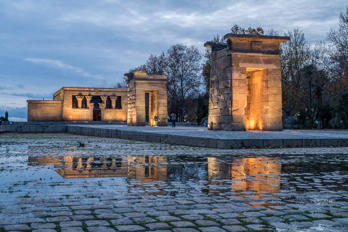 This image shows the Temple of Debod in the blue hour. The temple is lit and it's surrounded by an artificial pond.