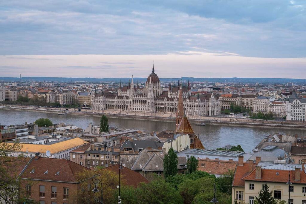 This image shows a panoramic view of Pest and the Danube River. The Hungarian Parliament is the dominant building in the photo. The photo was taken from the Fisherman's Bastion.