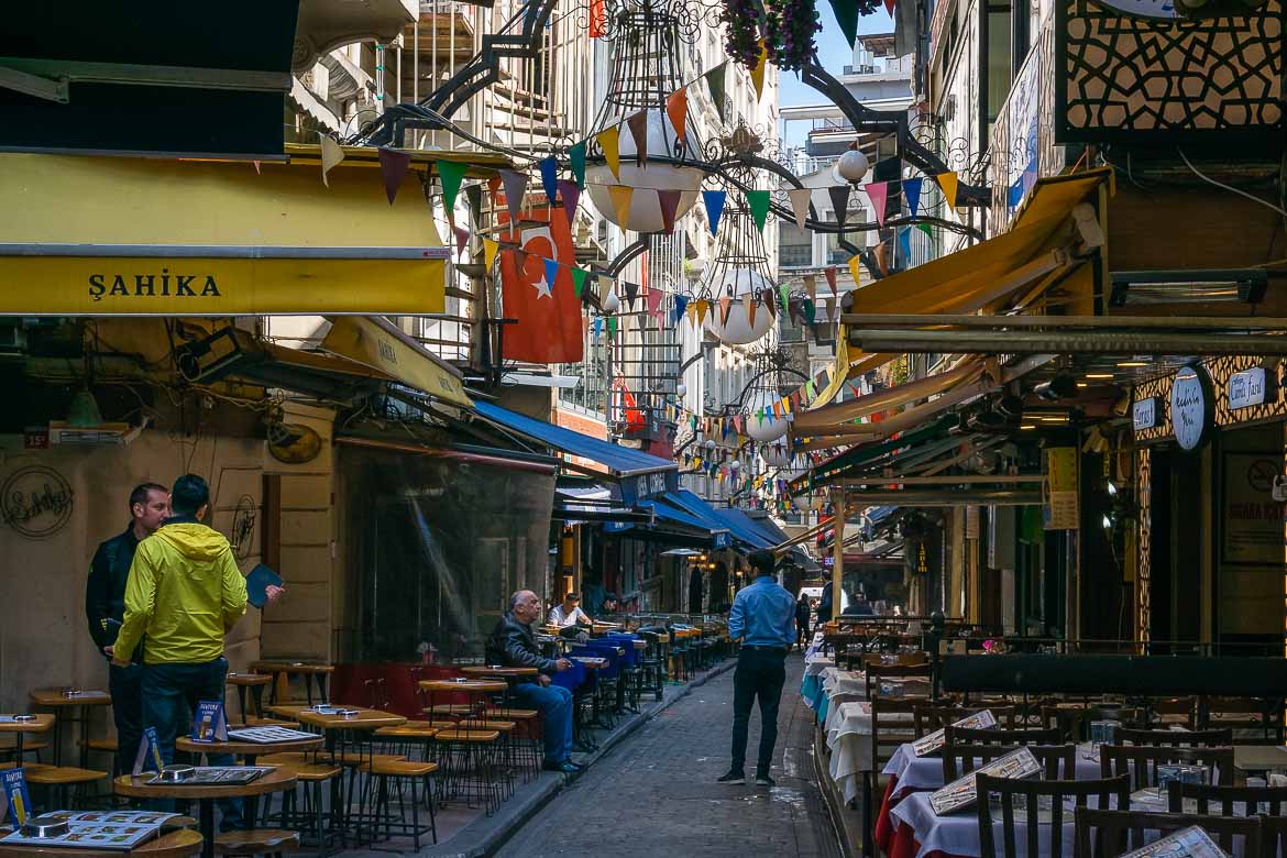 This is Nevizade Street. It is lined with tables and chairs, now empty, because this area comes to life in the evening. Colourful small flags and a big Turkish one hang above the street creating a festive ambiance.