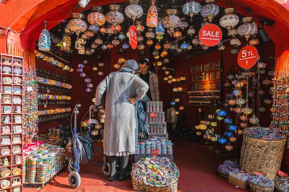 A shop that sells traditional colourful lamps. The walls inside are red and a woman is looking at the merchandise.