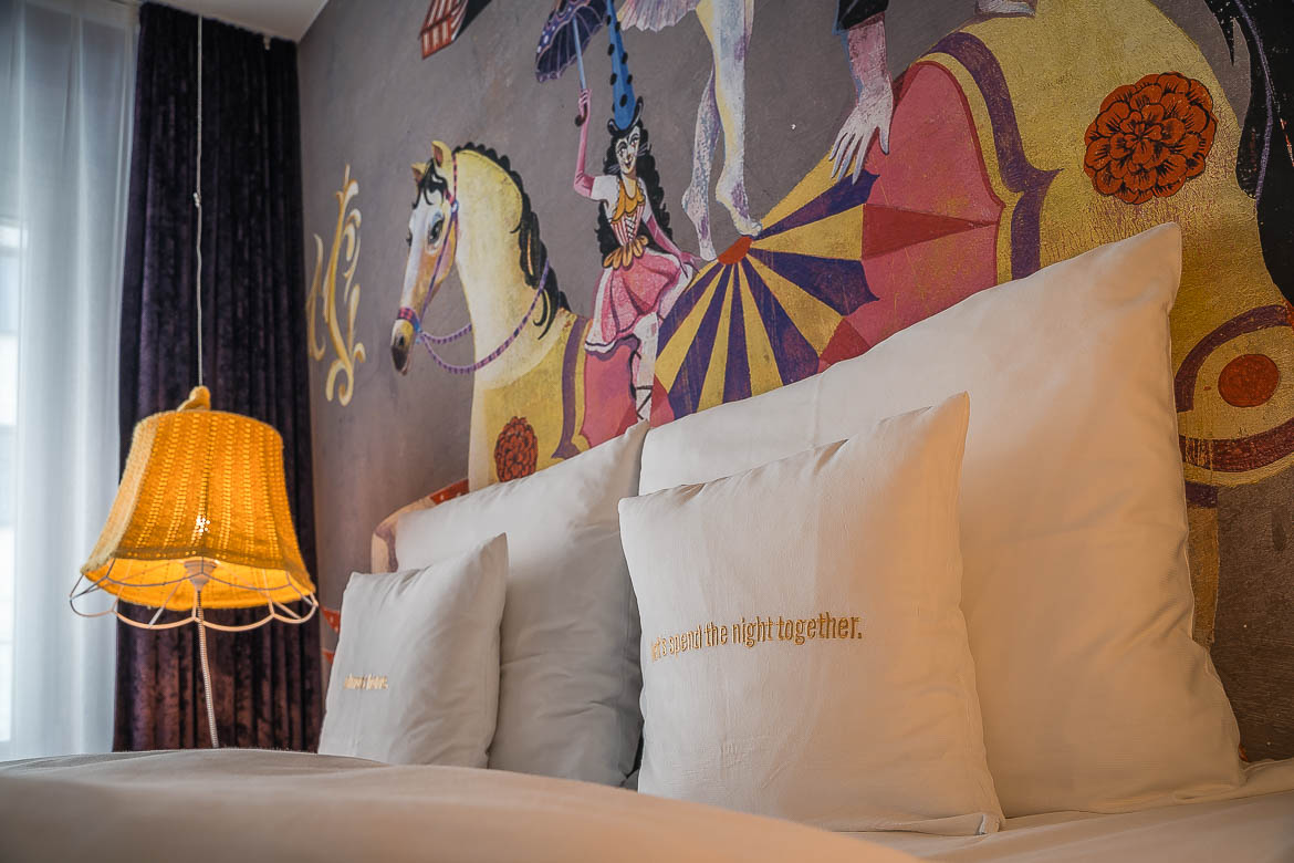 The bed in our room at 25hours Hotel. The pillows have a "let's spend the night together" sign. The wall over the bed has a circus-themed painting.