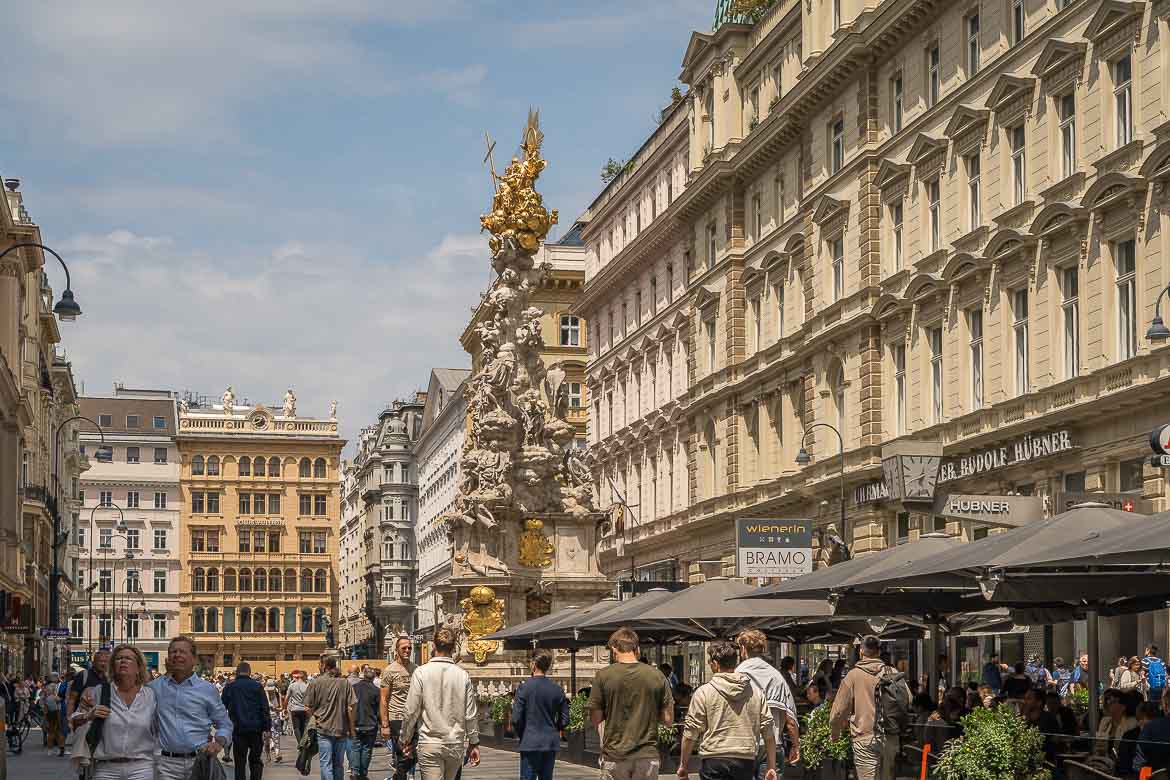 People walking on Graben Street. The Baroque Plague Column stands in the middle of the street.