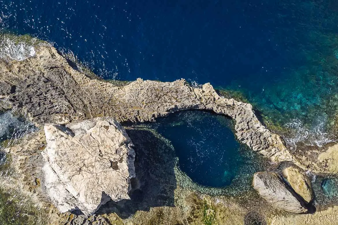 Top-down view of the Blue Hole from a drone. The Blue Hole is a round vertical tunnel in the sea, surrounded by rocks.