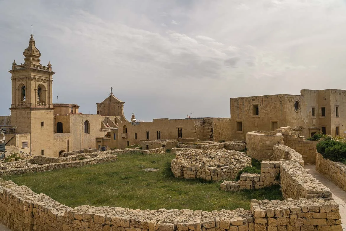 Ruins surrounded by walkways and old buildings in Gozo's citadel.
