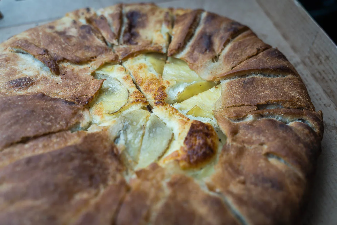 Gozitan Ftira in a box from the bakery. Ftira looks like a pizza with thick dough and it's filled with cheese and potatoes.