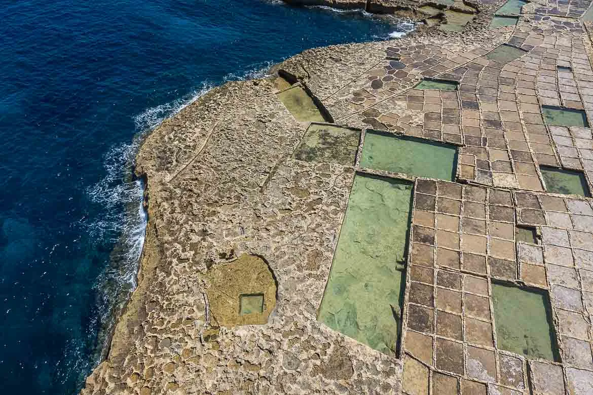 Panoramic view of Gozo's salt pans from a drone. Most of the pans are small square basins forming an impressive canva that is interrupted by larger rectangular pools. 