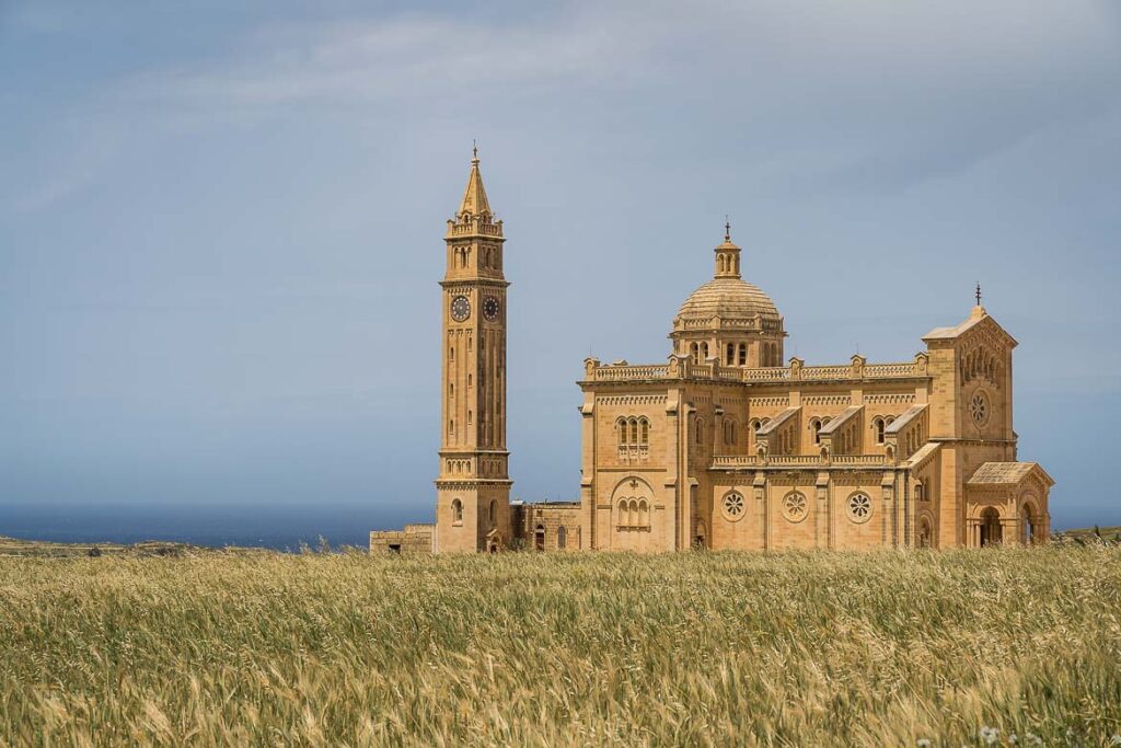 View of the Ta' Pinu Basilica from the street. The imposing basilica has terracota colour and the bell tower stands separately behind the main church.