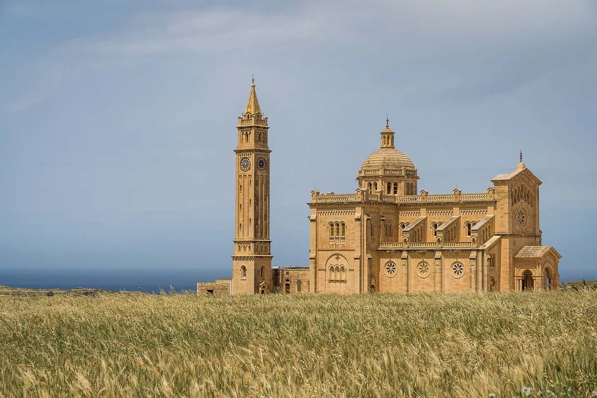 View of the Ta' Pinu Basilica from the street. The imposing basilica is of terracota colour and the bell tower stands separately behind the main church.