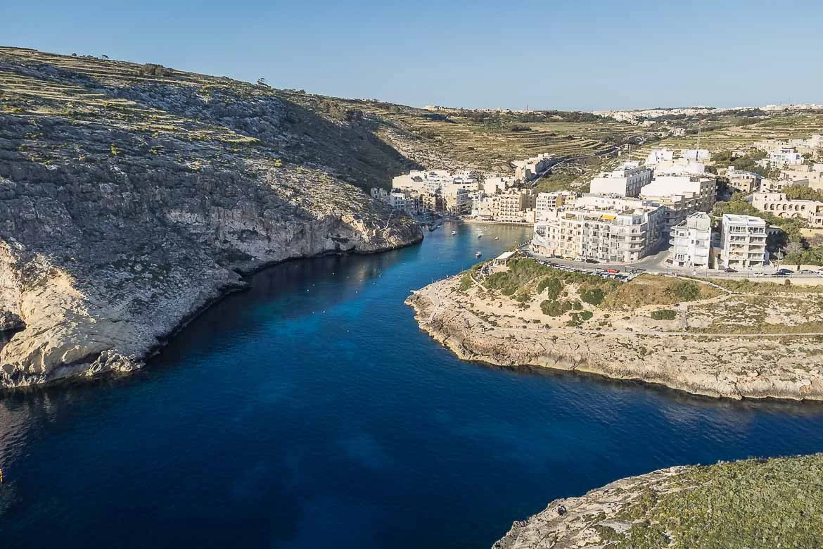 Panoramic view of Xlendi Bay from a drone. The sheltered bay is surrounded by big blocks of flats and hotels.