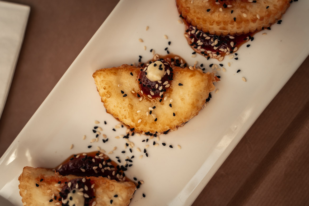 This image shows pieces of fried local cheese served with tomato jam and poppy seeds.