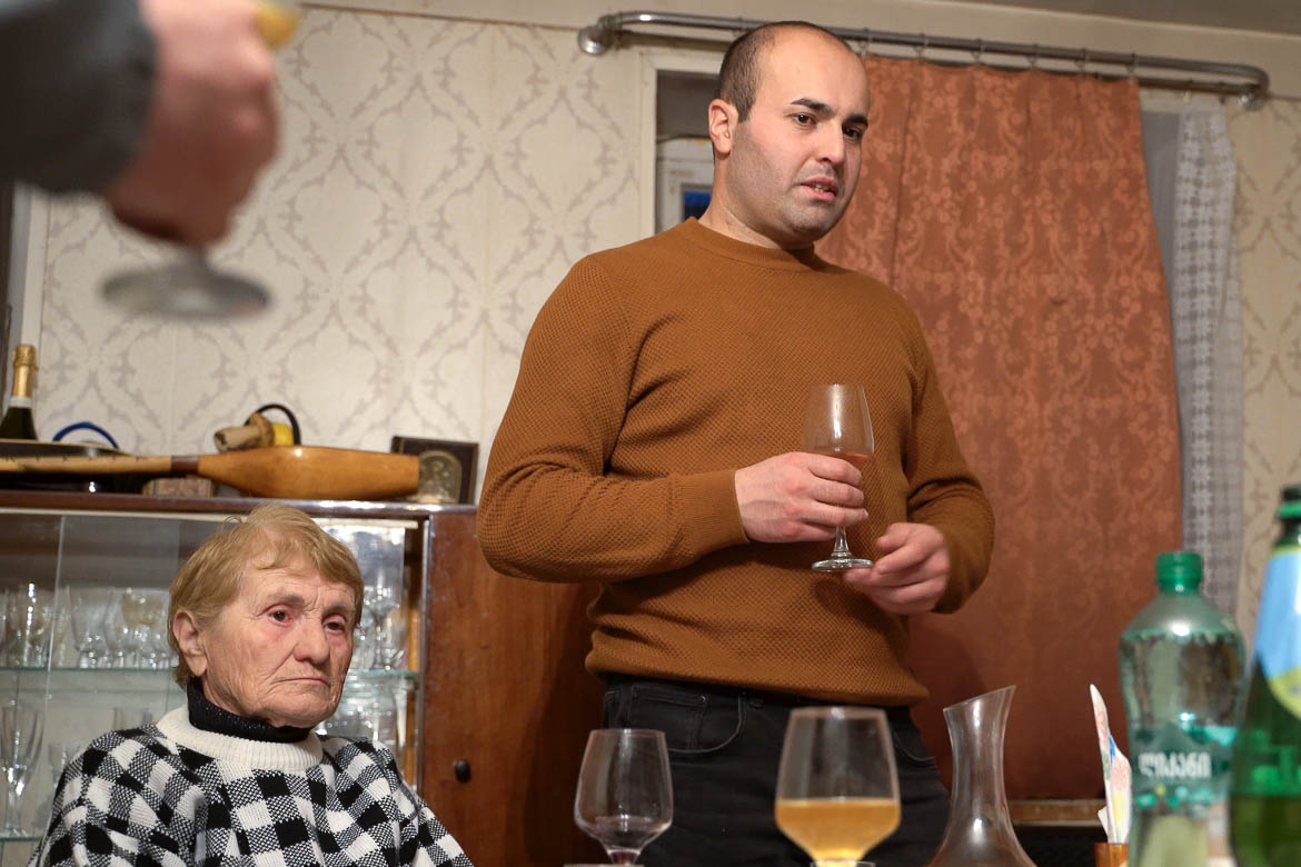 The tamada standing next to his grandmother, proposing a toast during the Georgian supra.