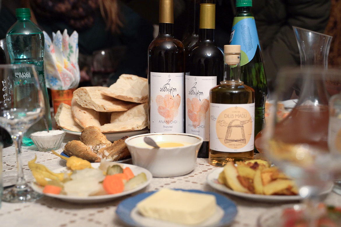 A table with dishes of food, two bottles of wine and a bottle of Georgian chacha.