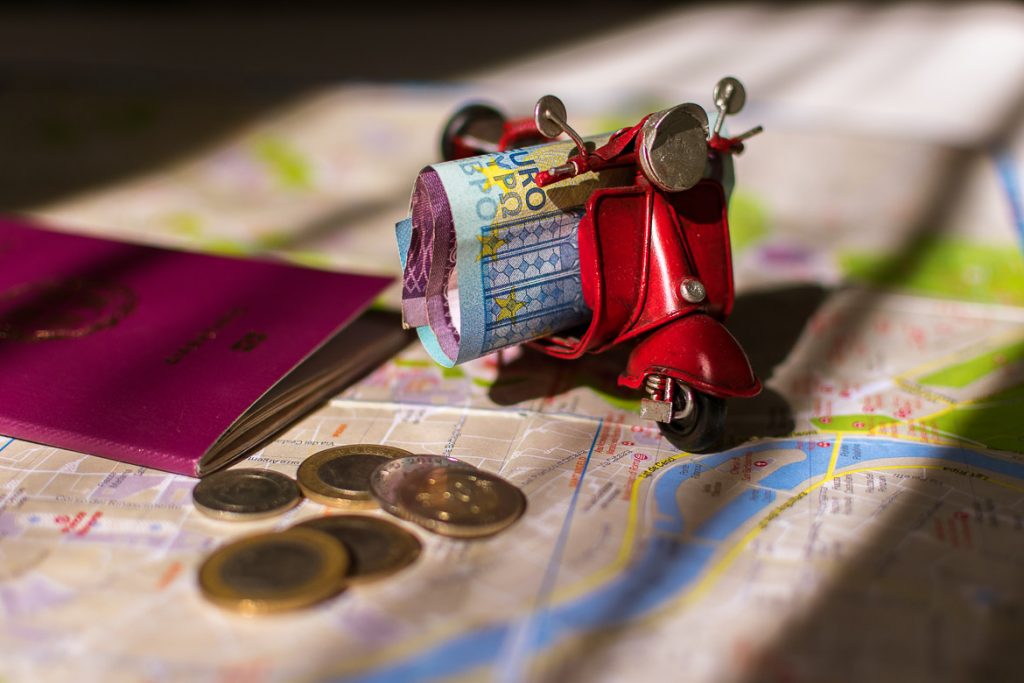 This photo shows a miniature vespa with money on it. There is also a map, a passpot and some coins. We've chosen this photo to be the featured image for our article: How to afford to travel often: Top 27 tips to save money.