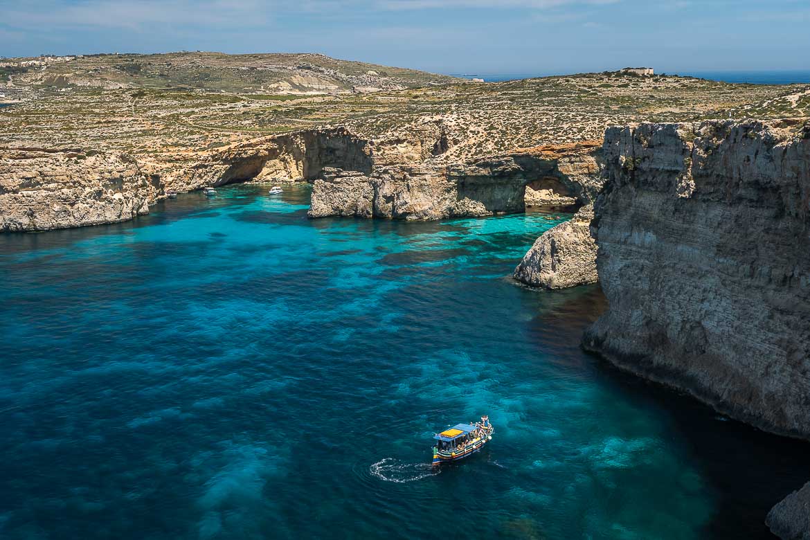 This image shows a panoramic view of the cliffs and sea of Comino, with a boat approaching the Crystal Lagoon.