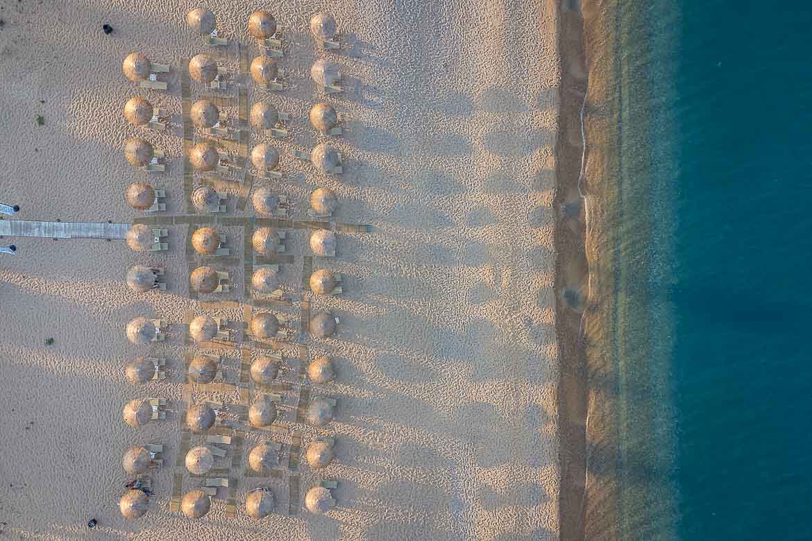 A top-down view of Skala beach from a drone. Four rows of umbrellas and sunbeds on the beach.