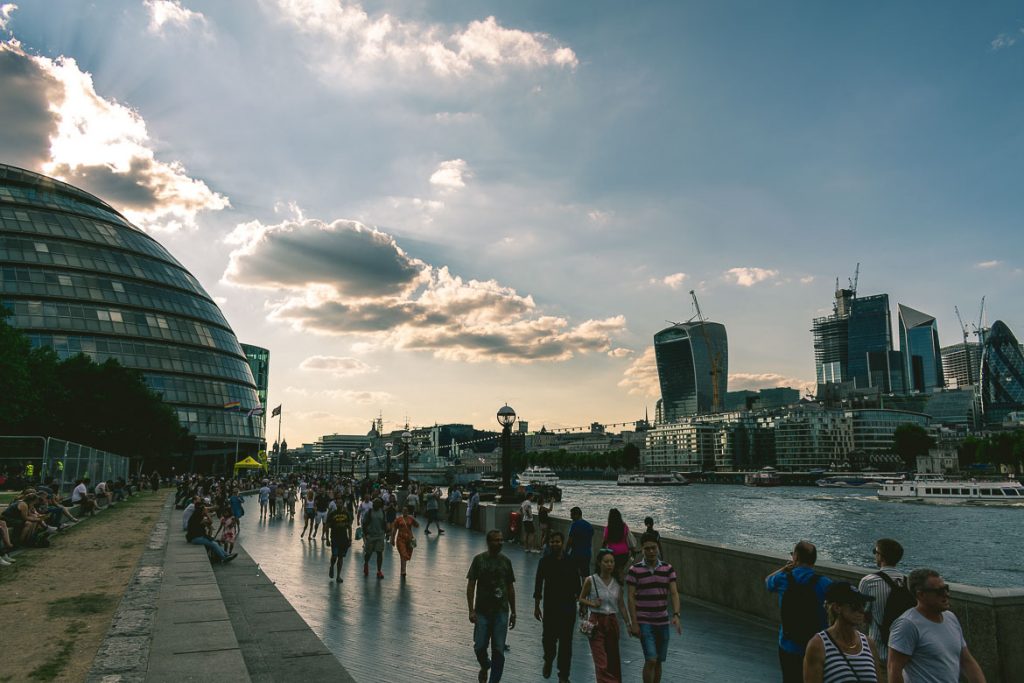 This photo shows the Thames South Bank at sunset. People walking in front of the City Hall in London, England. This is our favourite South Bank walk.