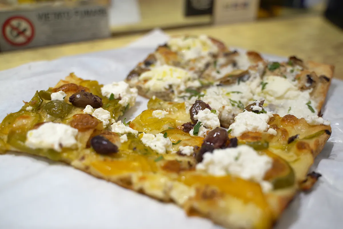 A close-up of Pizza al Taglio topped with olives and ricotta cheese.