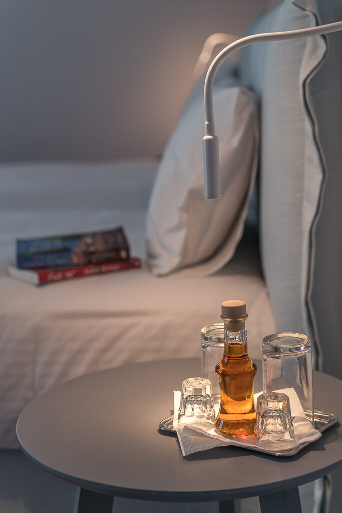 This image shows the bedside table with a bottle of psimeni raki on it at Vigla Hotel in Amorgos.
