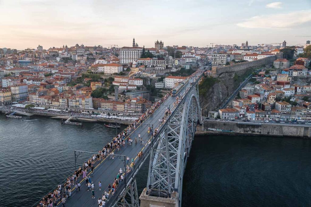 View of Ponte Luis and Porto from Mosteiro da Serra. People walk along the side edges of the upper deck as the metro crosses the bridge.