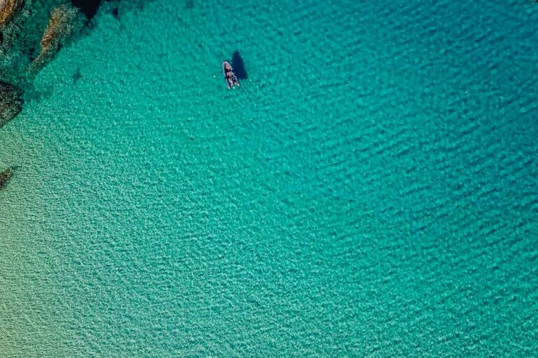 Top down shot from a drone of the sea in Serifos. A small boat floats on the turquoise waters.
