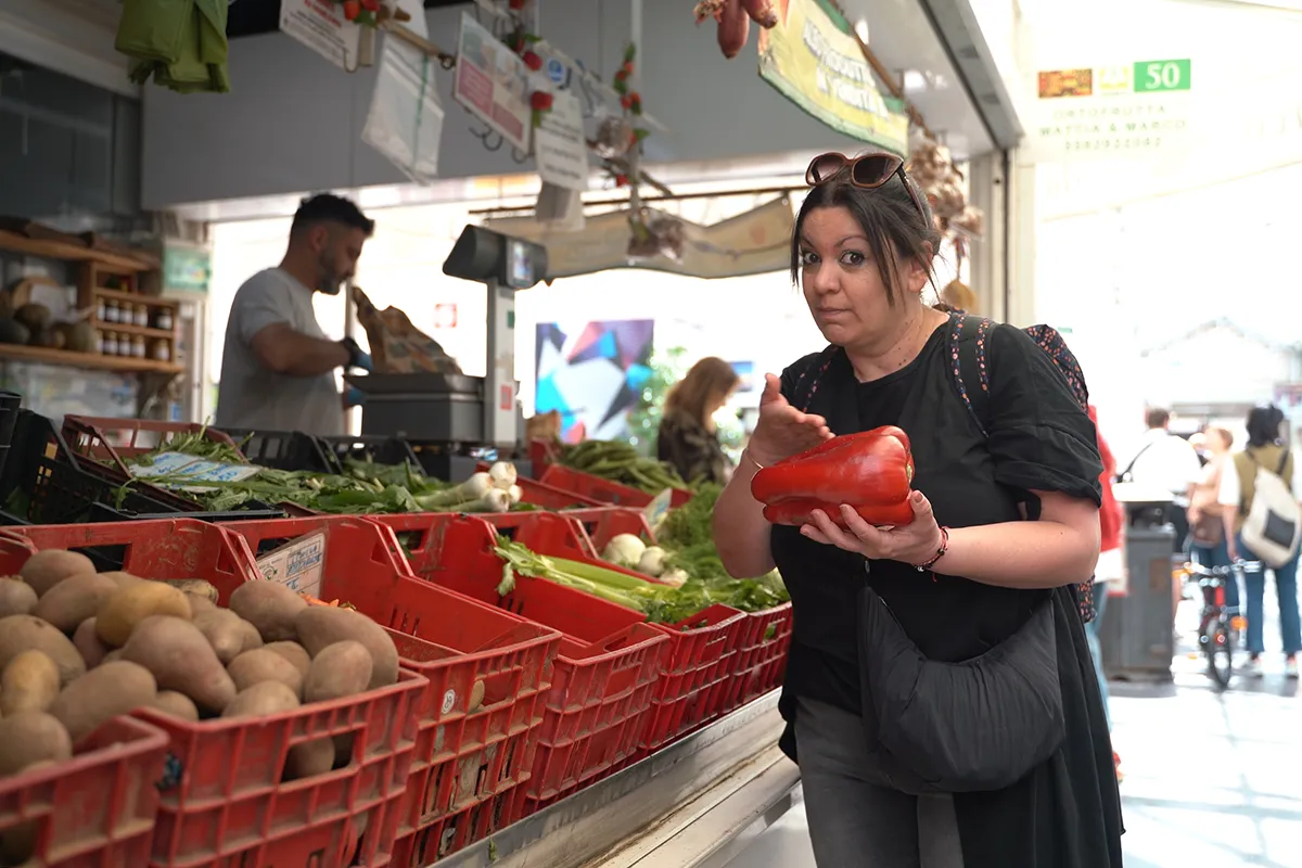 Maria holding and showing off a huge red bell pepper at the market.