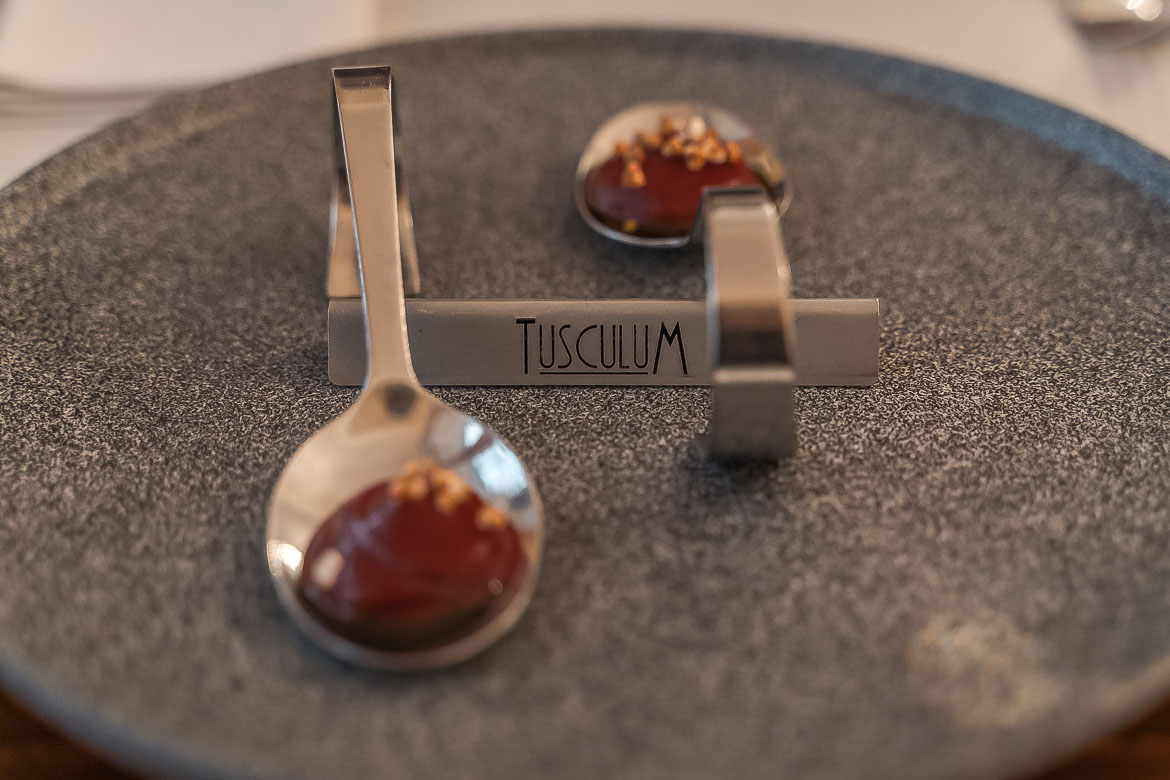 The welcome dish at Tusculum restaurant. Two spoons filled with red sauce on a plate. In the middle of the plate there's a sign with the restaurant's name on it.