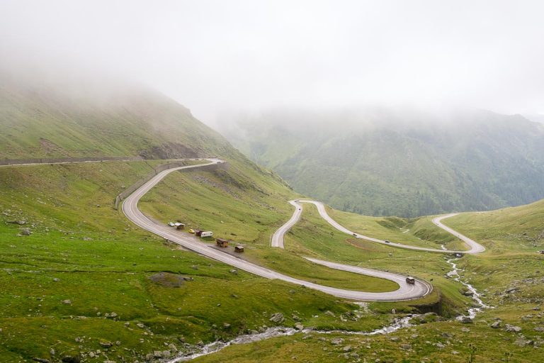 This photo shows the hairpins of the Transfagarasan on a green setting with the fog looming over the mountain tops.