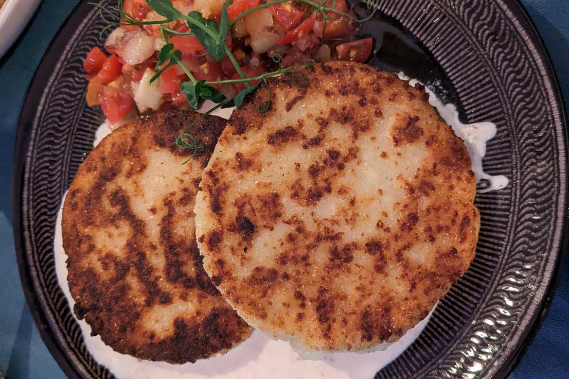 A close up of two fried cornbreads placed over a layer of white sauce. 