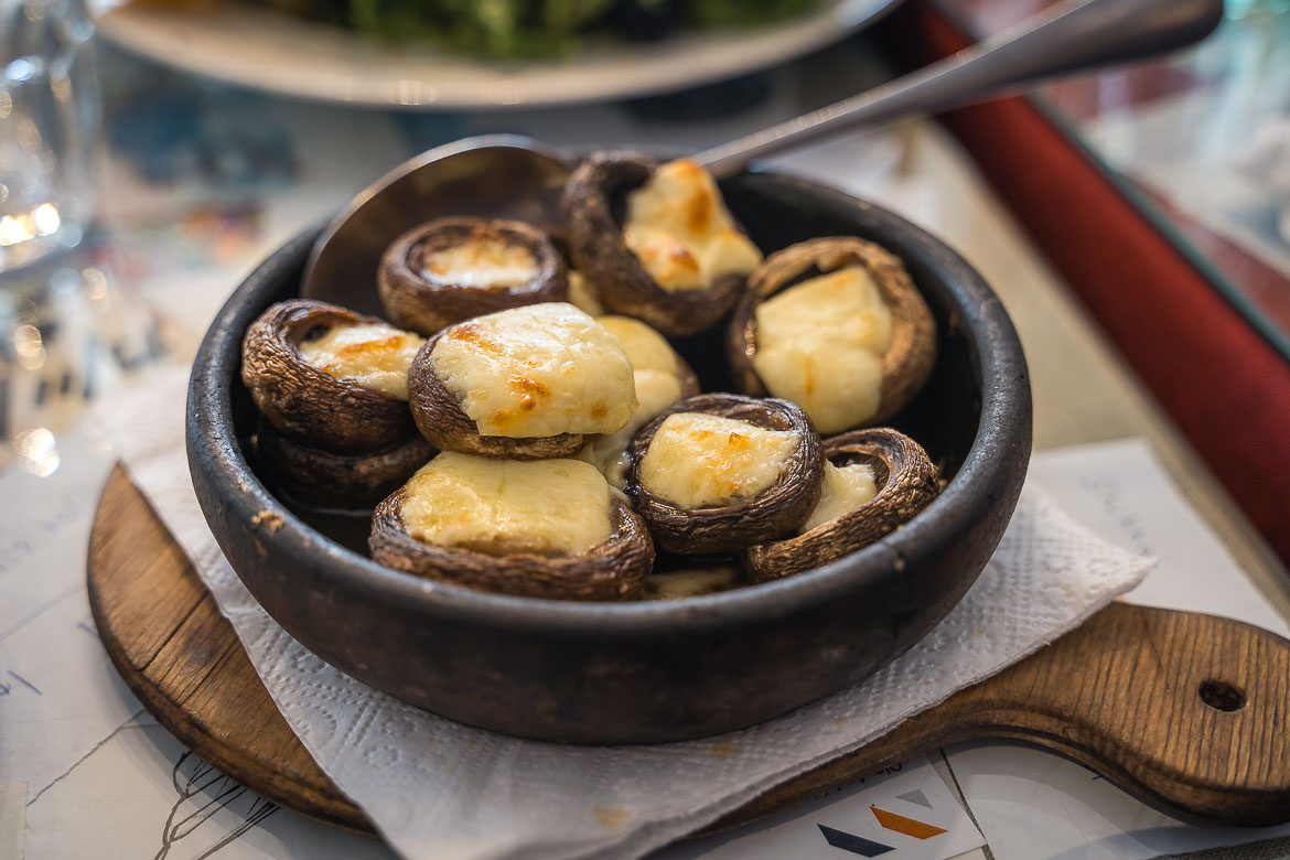 A close up of a clay pot with mushrooms filled with cheese. 