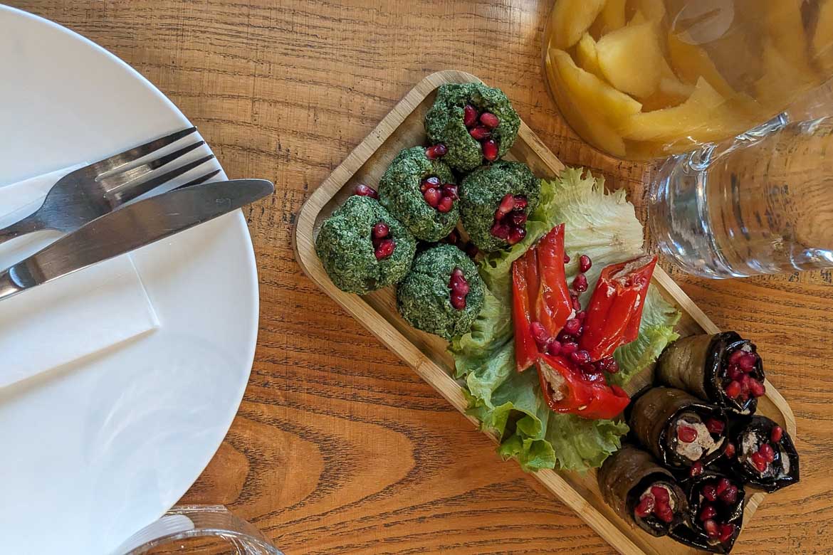 A wooden dish with green Pkhali and Nigvziani Badrijani.  