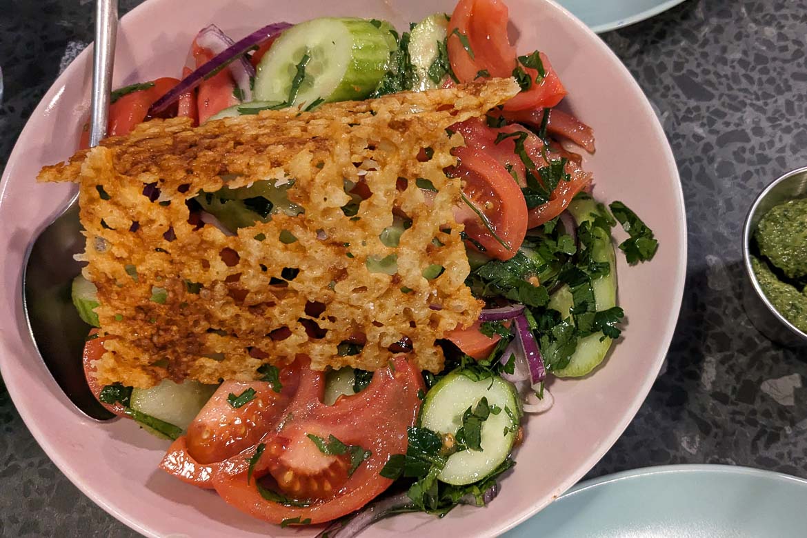A close up of a salad with tomatoes, cucumbers, fresh herbs and toasted cheese. 