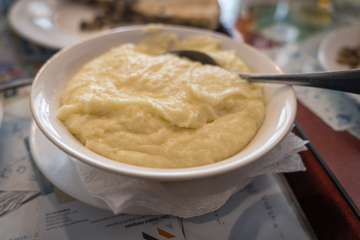 A close up of a white bowl of Tashmijabi, thick mashed potatoes with cheese. 