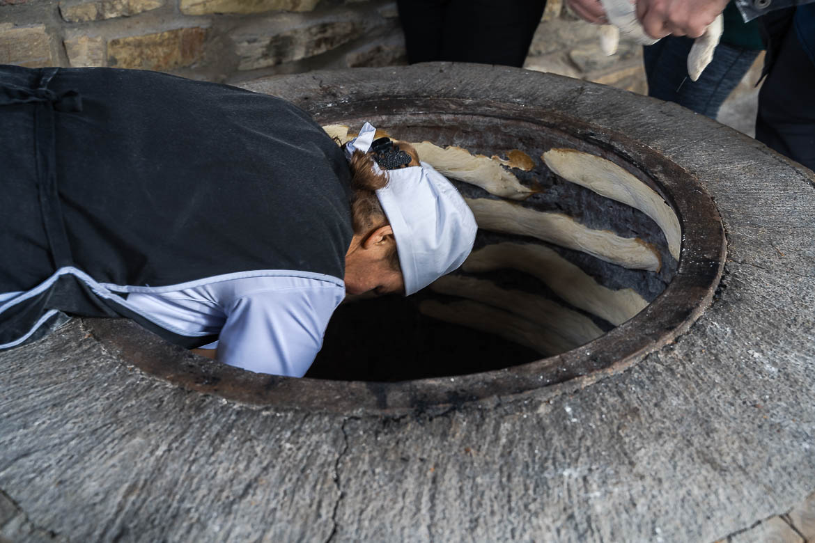 A woman leaning inside a well-shaped oven to place pieces of dough. 