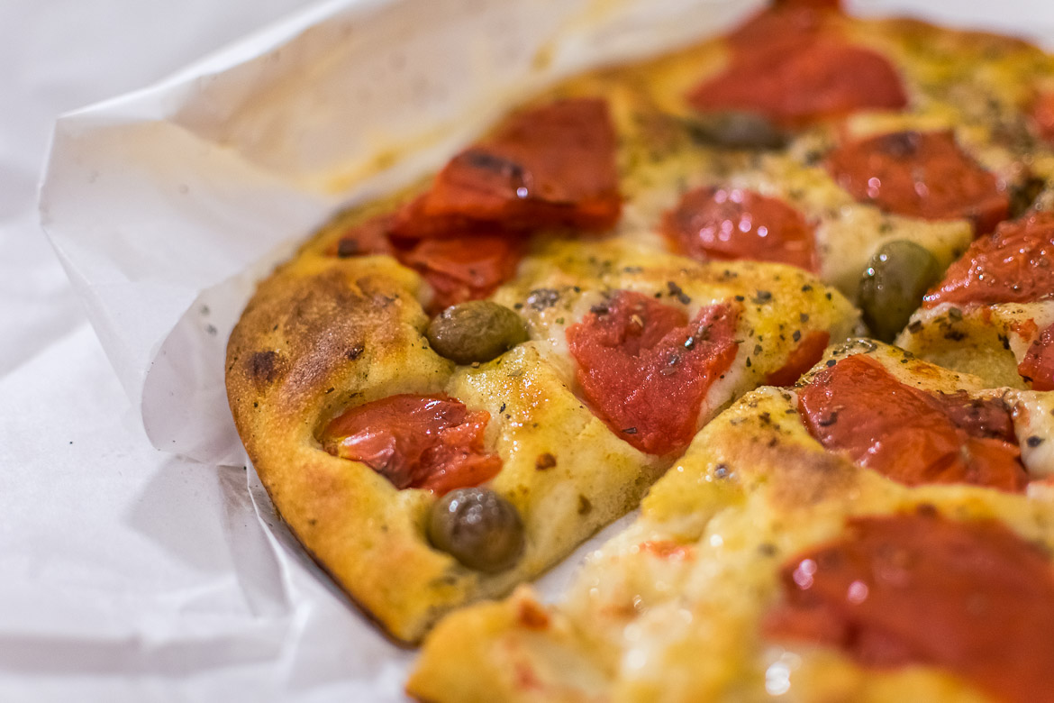 This is a close up of focaccia barese which looks (and was) outrageously delicious. The focaccia is topped with fresh tomato and green olives.