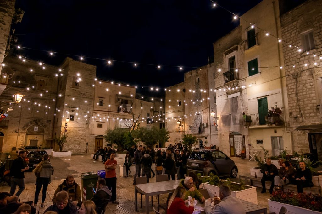 What To Do in Bari Italy: A Full Guide To Puglia’s Capital This image shows Largo Albicocca at night. There are people standing or sitting and there are lines of lights hanging above. The ambience is unique. This is why we chose this photo to be the feature image of our article: What to do in Bari Italy. A full guide to Puglia's capital.