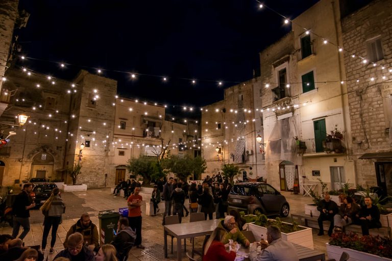 This image shows Largo Albicocca at night. There are people standing or sitting and there are lines of lights hanging above. The ambience is unique. This is why we chose this photo to be the feature image of our article: What to do in Bari Italy. A full guide to Puglia's capital.