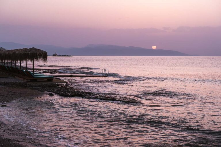 This image shows the sea on Skala Beach dyed purple and the sun setting in the background. This is the featured image for our article What to do in Agistri, the best island near Athens.