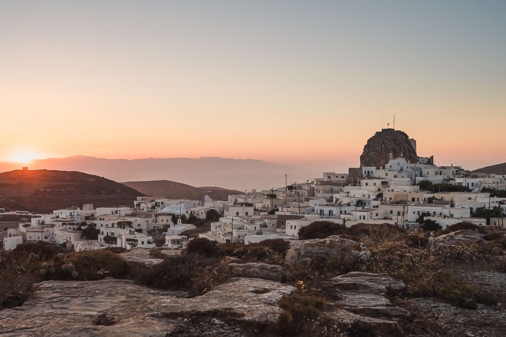 What To Do in Amorgos, Our Favourite Greek Island This is a panoramic shot of Chora at sunset, taken from the windmills. The sky is orange and the buildings are whitewashed. You can see the sea in the background. This is the featured image for our article: What to do in Amorgos Greece.