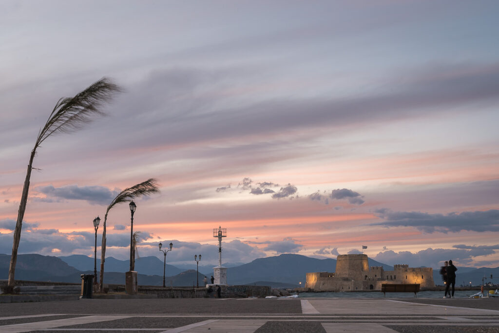 What To Do in Nafplio, The First Capital of Greece This image shows the lit Bourtzi Fortress during sunset on a windy day.