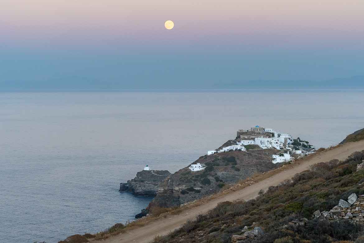This photo shows Kastro as seen from Verina Astra Hotel. The sky is light blue and lilac and there is a huge full moon above. Kastro is one of the most iconic places to visit in Sifnos.