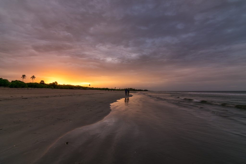 What To Do in Trincomalee on Sri Lanka’s East Coast This photo shows Nilaveli Beach at sunset. There are two people walking on the sand and the sky is cloudy. Yet there are beautiful yellows and oranges in the sky. We chose this photo to be the featured image of our article What to do in Trincomalee Sri Lanka in 2 days.