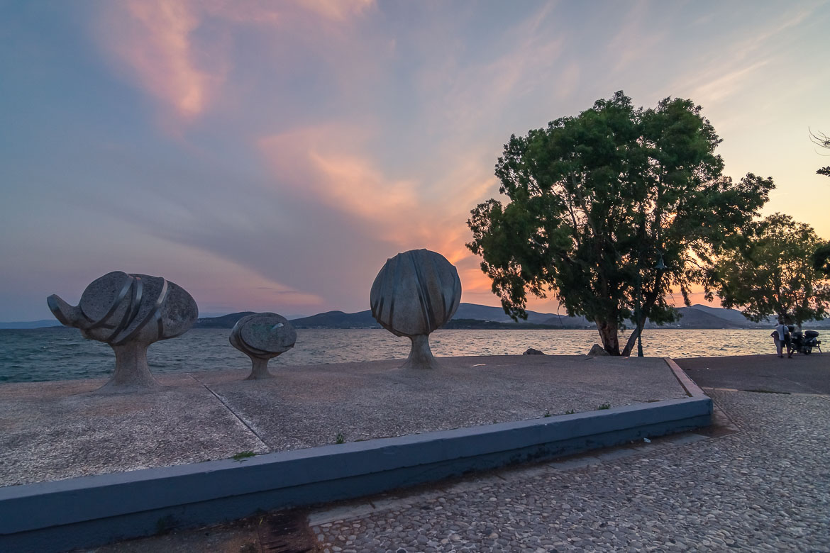 This image shows the strange-looking sculptures of Philolaos at Anavros Park. In the background, the sea and a gorgeous sunset.